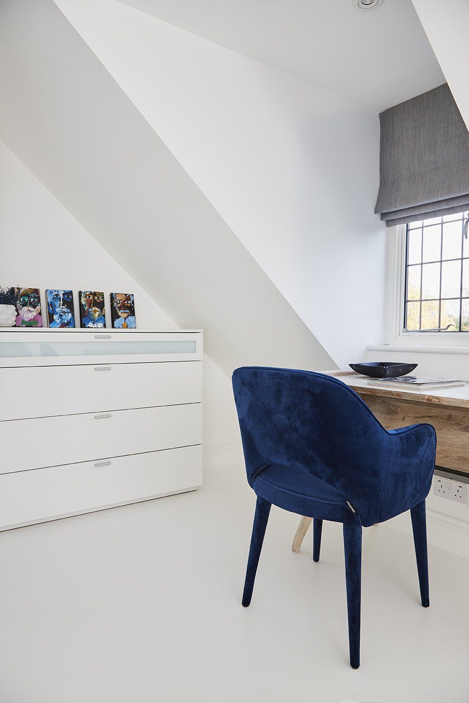 Blue chair at a white desk in a bright room with a slanted ceiling and window.