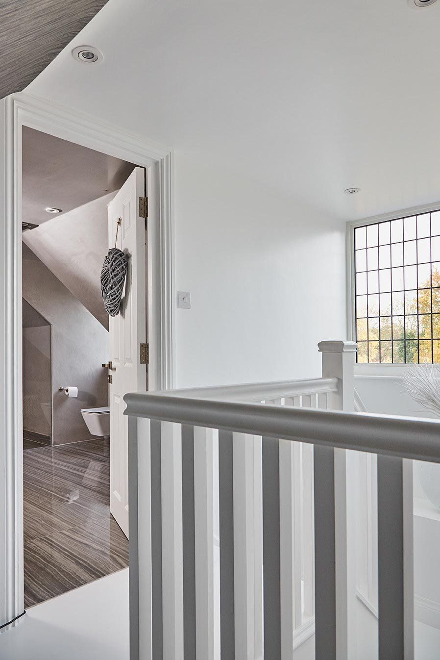 Bright white hallway with a stair railing, open doorway, and a window with bars