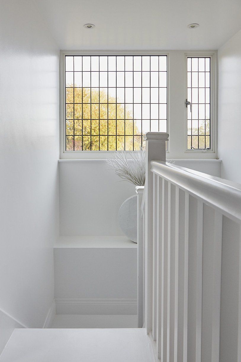 White stairway landing with a barred window and railing, showing soft daylight and a glimpse of trees outside