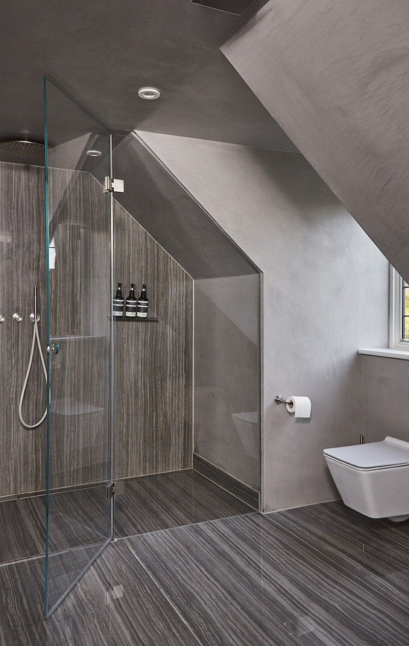 Modern bathroom with sloped ceiling, glass shower, wood-look wall, gray tile floor, and wall-mounted toilet