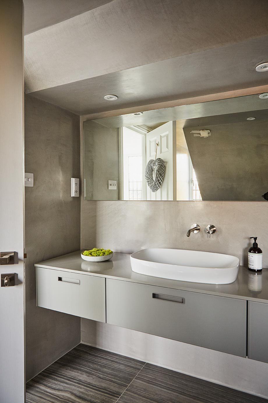 Modern bathroom with floating gray vanity, white sink, large mirror, and striped floor rug