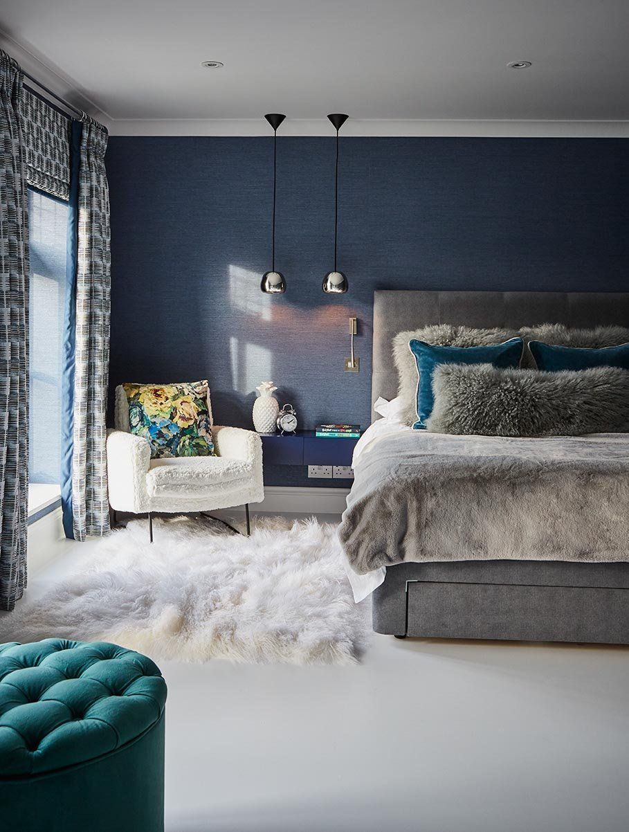 Stylish bedroom with navy accent wall, gray bed, teal chair, and fluffy white rug