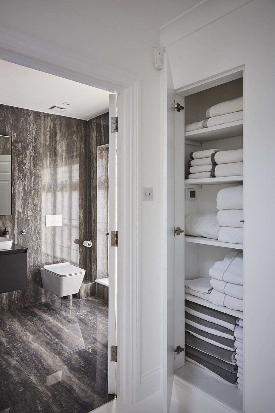 Bathroom with open linen closet holding neatly folded white towels and shelves beside a doorway