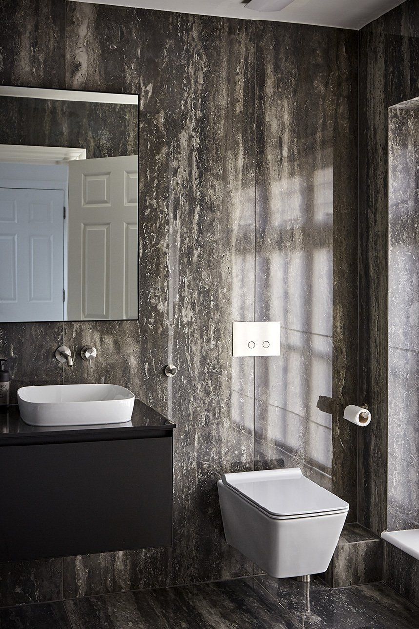Modern bathroom with dark textured walls, floating sink, wall-mounted toilet, mirror, and shower area