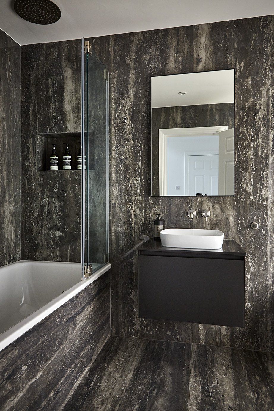 Modern black-tiled bathroom with bathtub, wall mirror, and floating sink cabinet
