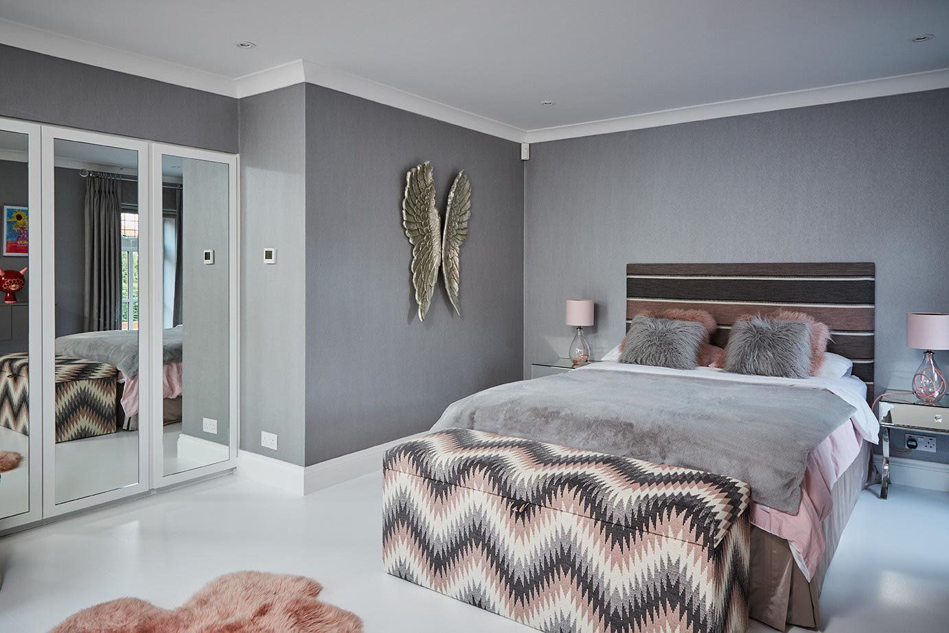 Modern bedroom with gray walls, mirrored closet, and a bed with patterned bedding and pink accents