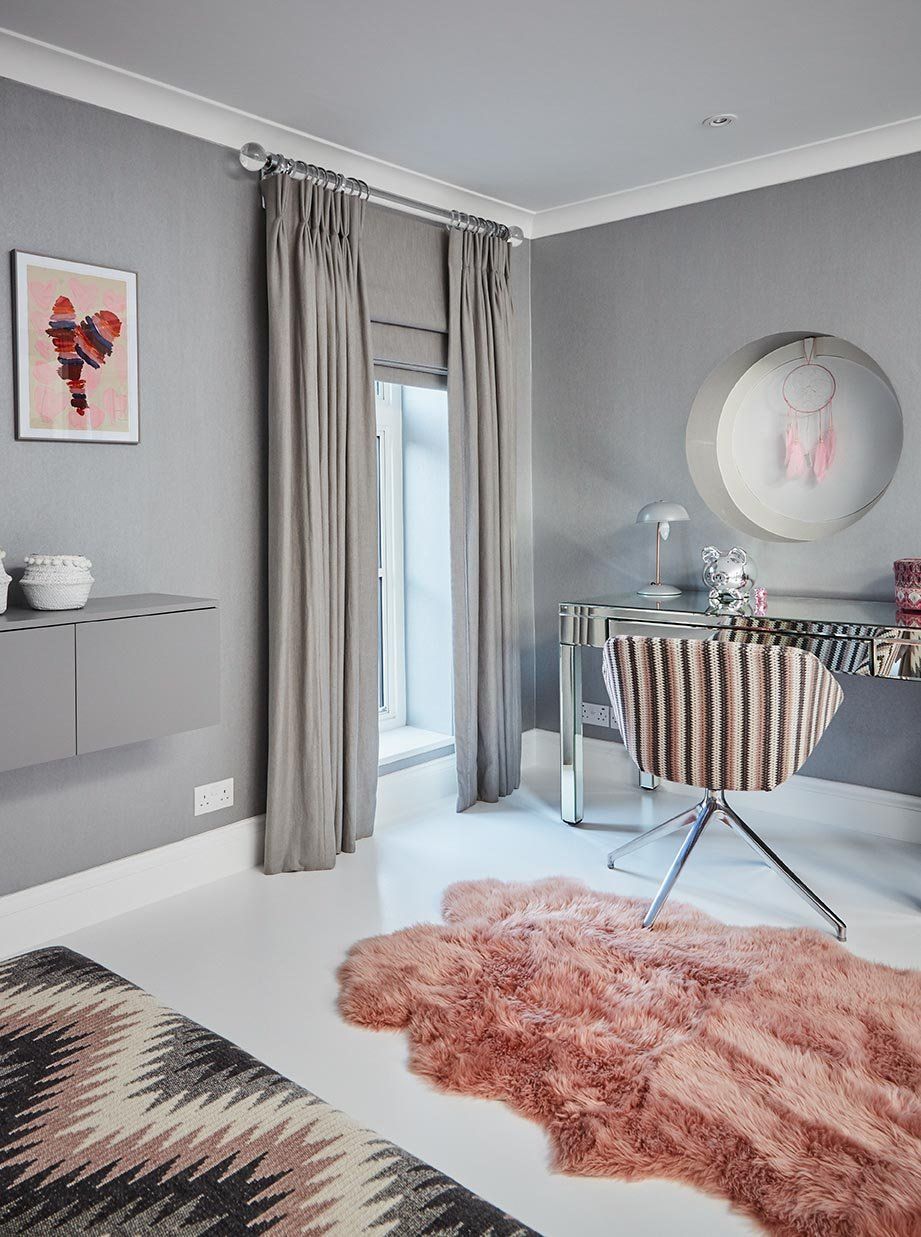 Modern gray bedroom with a pink rug, patterned chair, round wall art, and a small table by the window