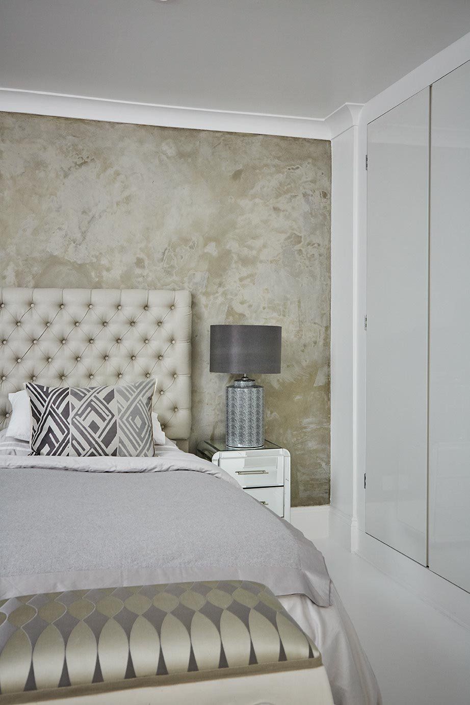 Elegant bedroom with tufted headboard, gray bedding, bedside lamp, and mirrored closet doors