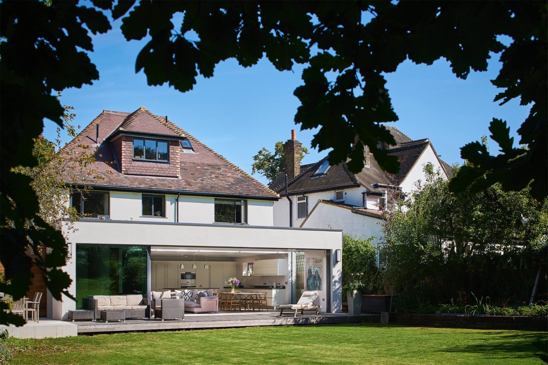 Modern white house with a red-tiled roof and large glass patio doors, seen from a lush garden
