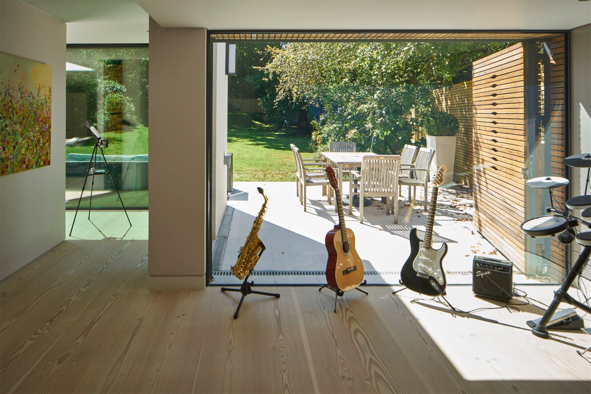 Open patio doors to a sunny backyard, with guitars on stands in a modern living room.