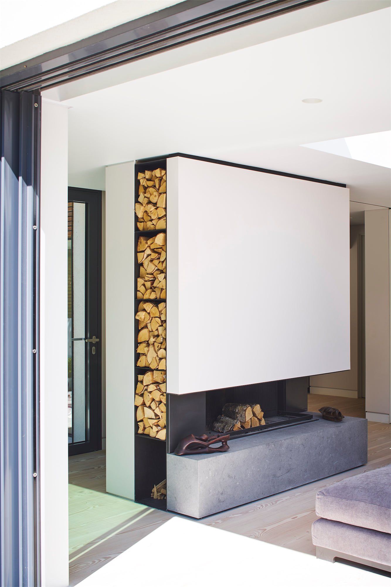 Modern living room with a white fireplace, stacked firewood, and sliding glass doors