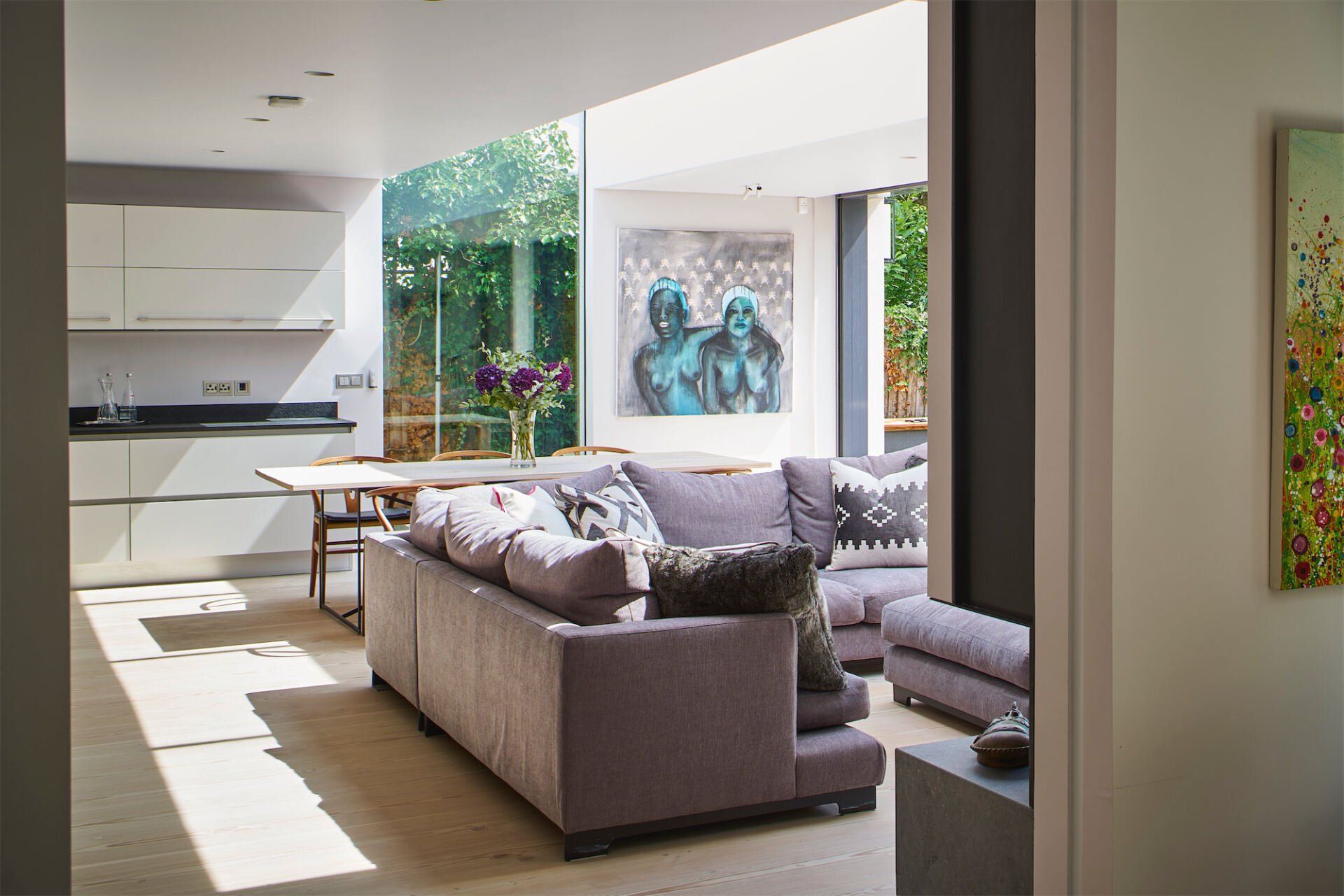 Modern living room with sectional sofa, large windows, and a bright open view into the kitchen and patio.