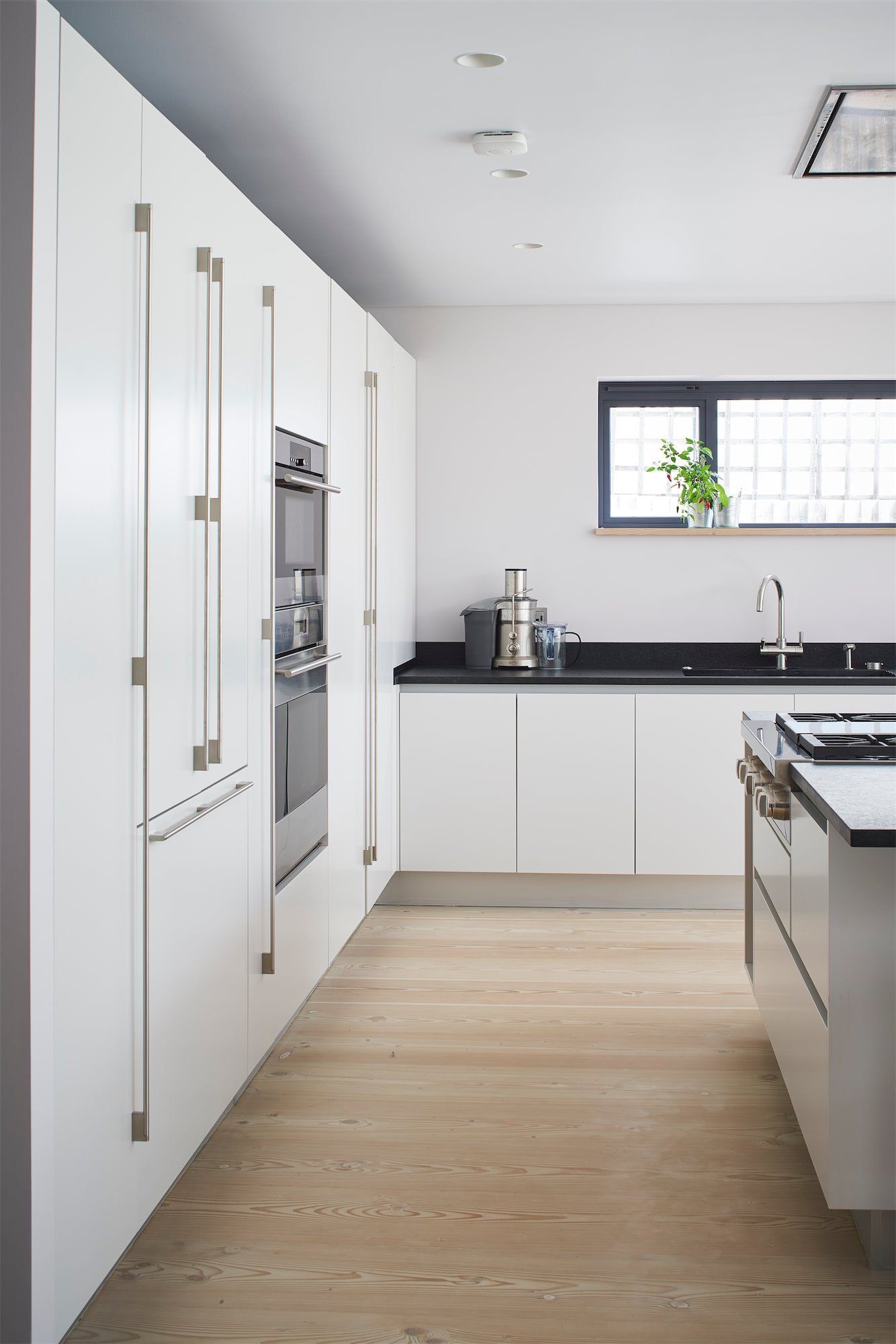 Modern white kitchen with island, black countertop, built-in appliances, and window light