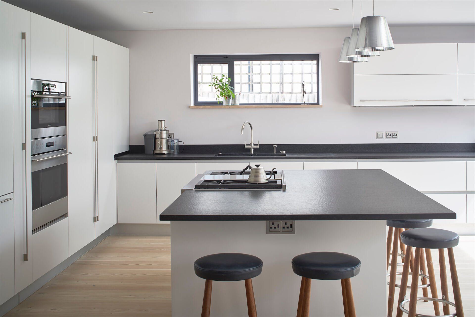 Modern white kitchen with black countertops, island stools, and a window above the sink