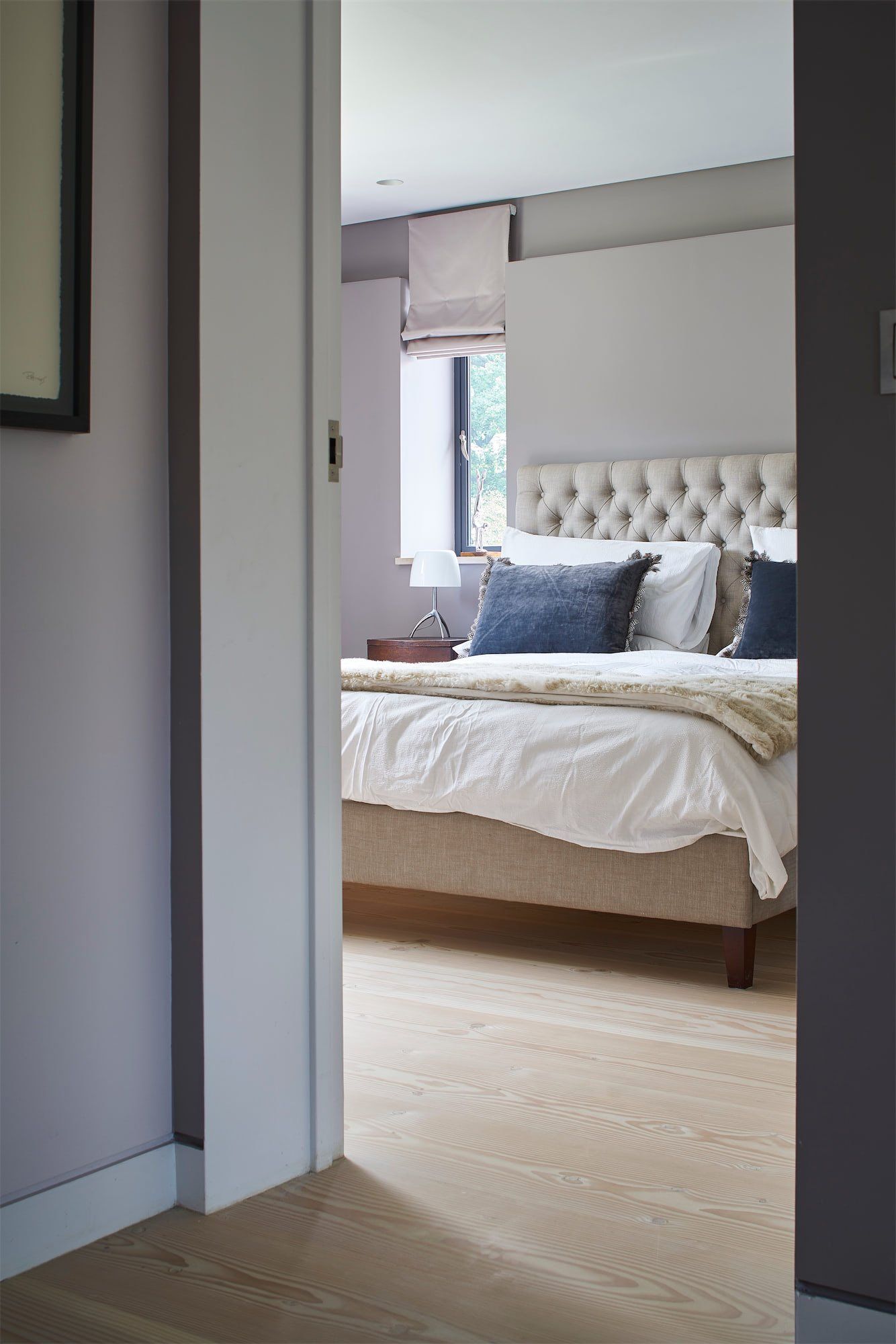 Bedroom viewed through an open doorway, with a tufted bed, white bedding, and a blue accent pillow.