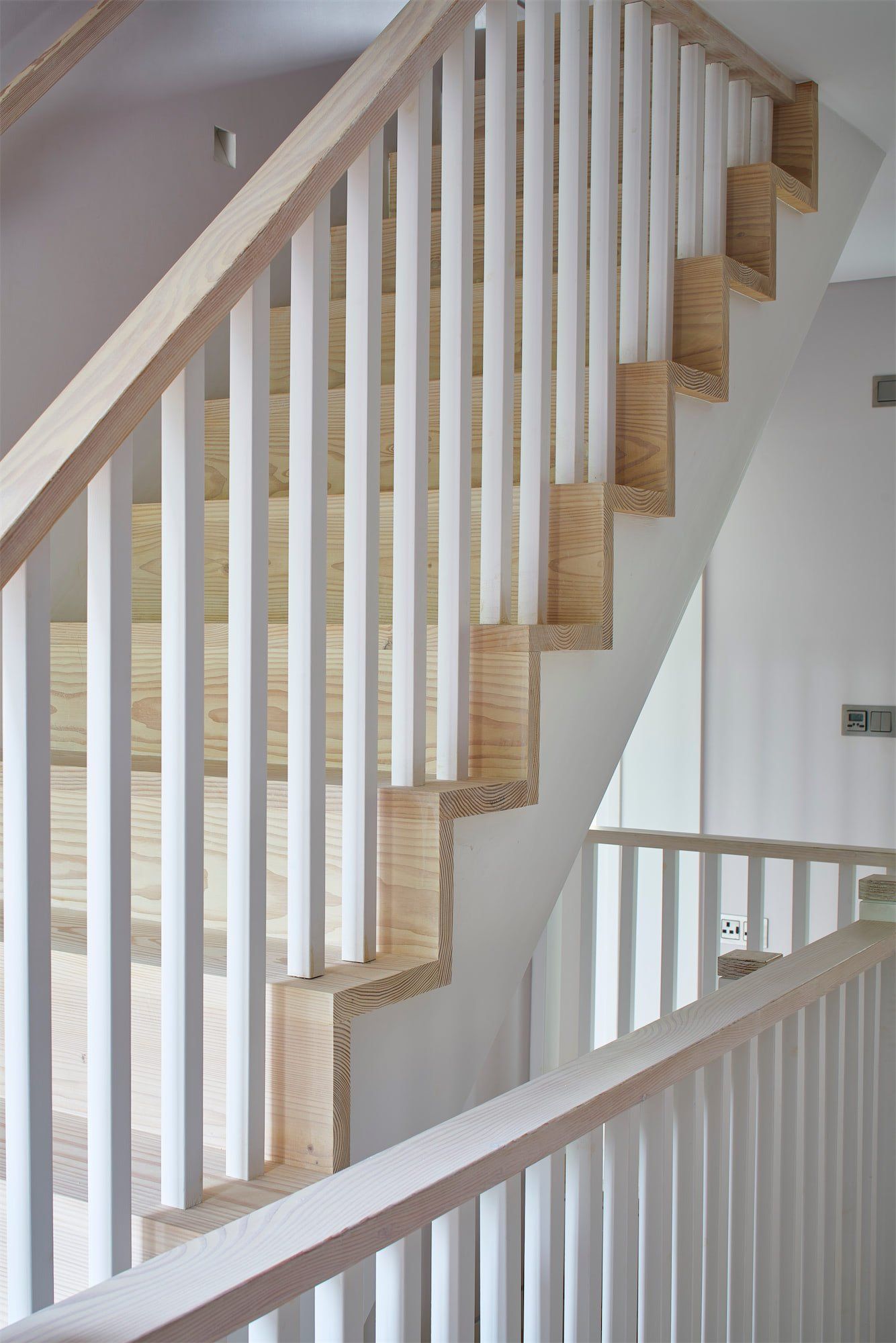 Indoor staircase with white railings and carpeted wooden steps on a light gray wall.