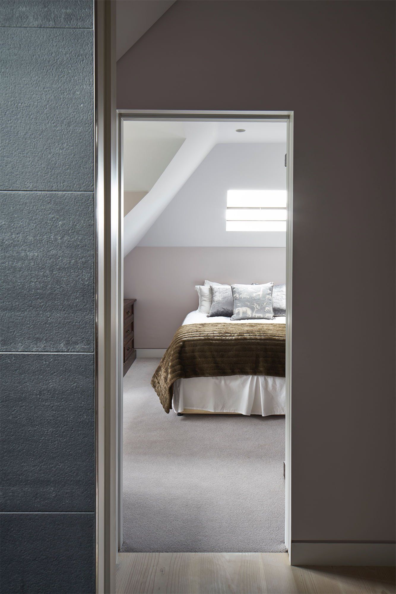 Bedroom seen through an open doorway with a neatly made bed and small window skylight.