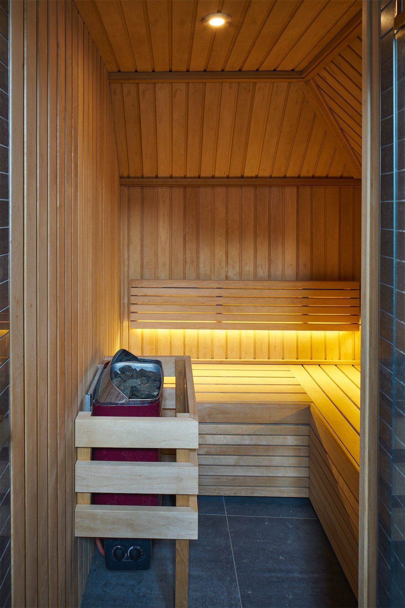 Wood-paneled sauna interior with benches, warm lighting, and a towel on the left bench