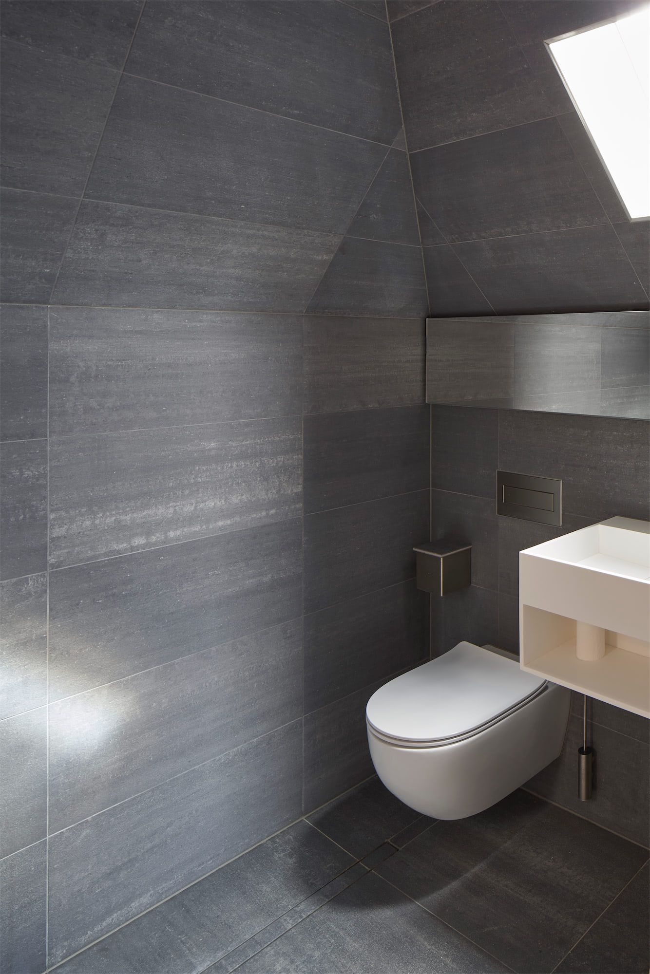 Modern gray bathroom with wall-mounted toilet, sink, and skylight.