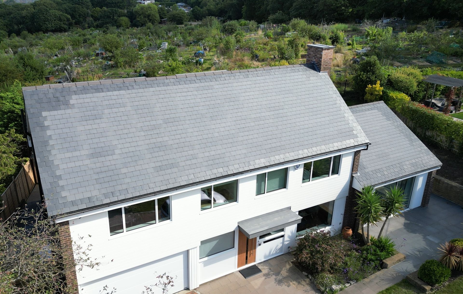 Aerial view of a white house with a gray roof, surrounded by trees and a driveway