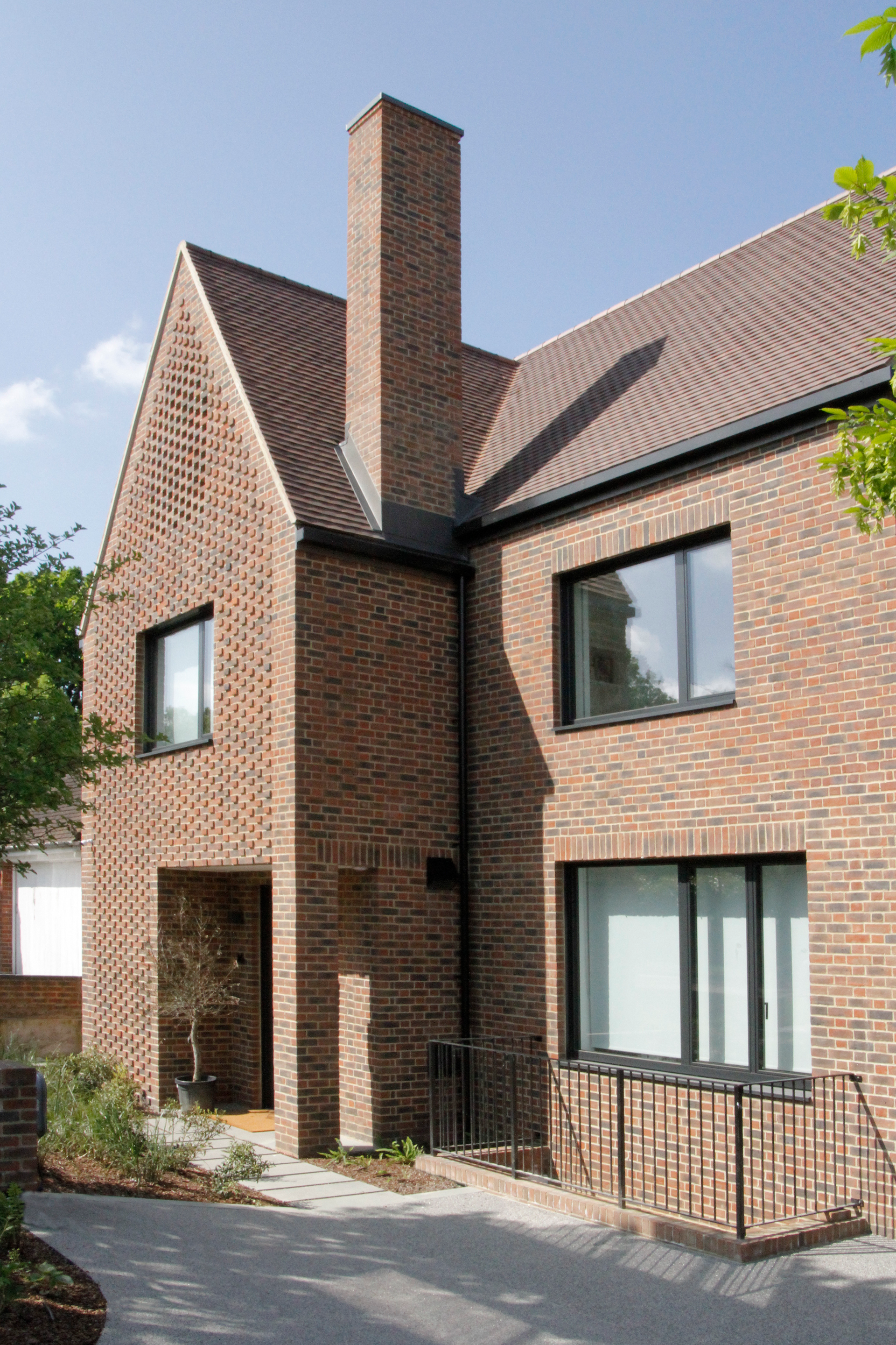 Brick house exterior with steep roof, chimney, and large windows on a sunny day