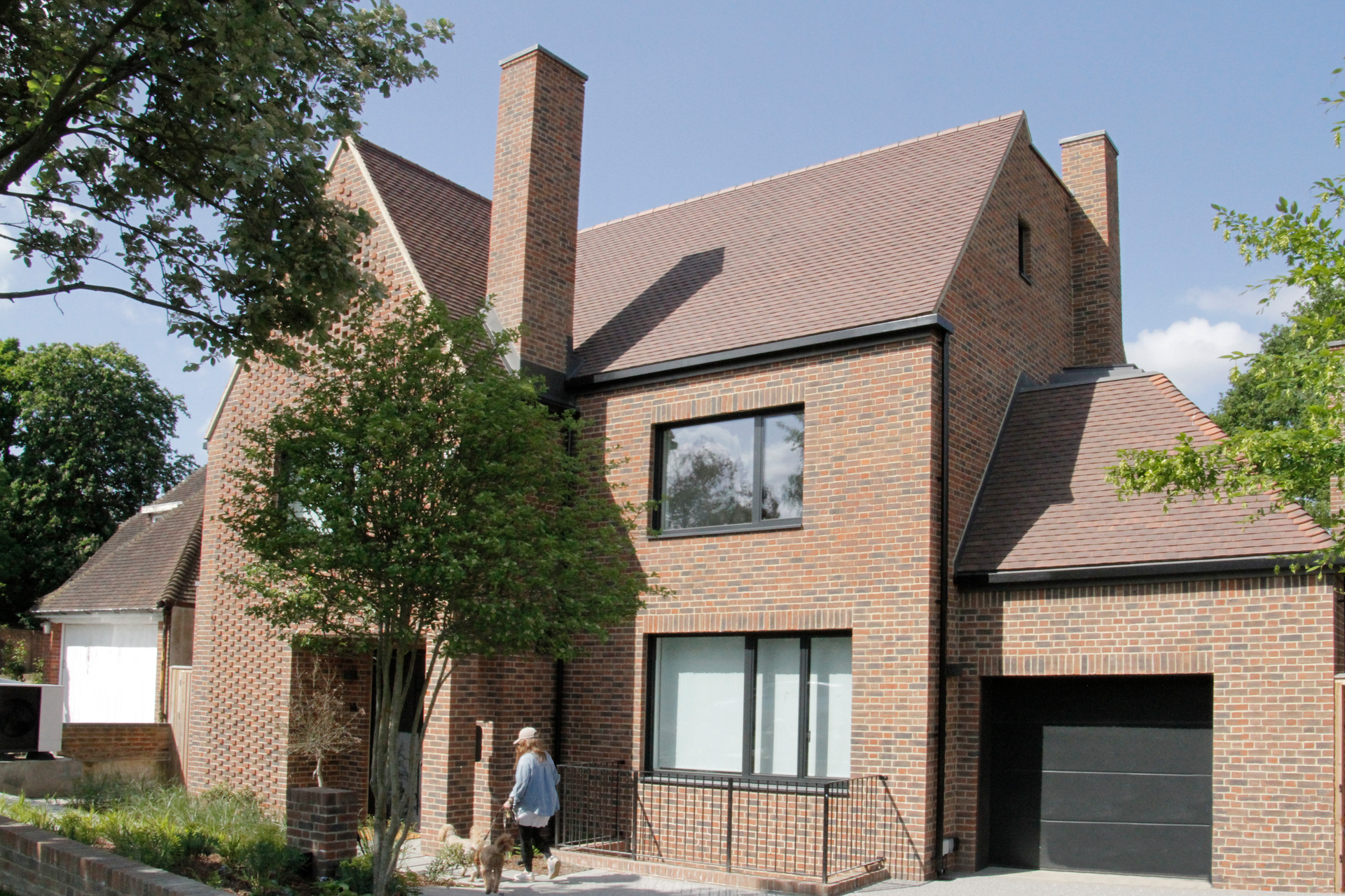 Brick house exterior with a steep roof, garage, and a person standing near the front entrance