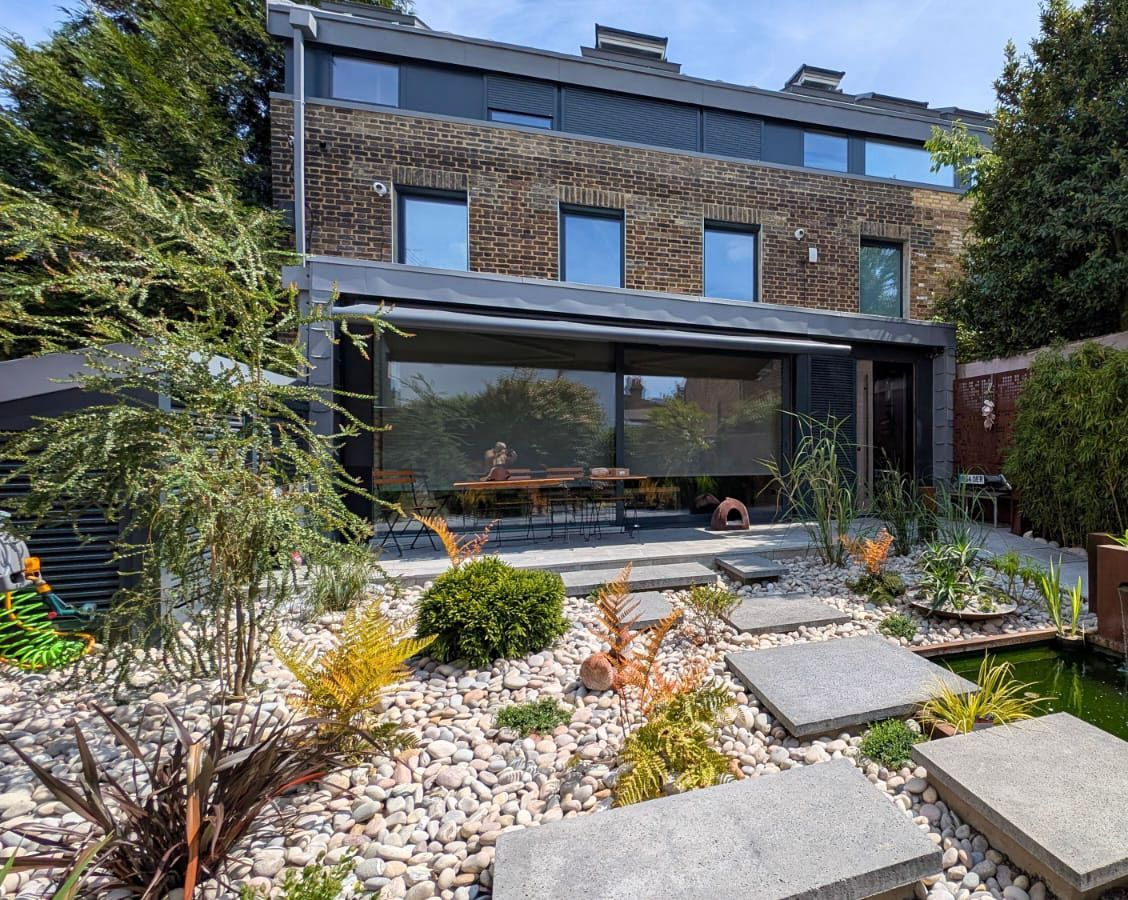 Modern brick house with a shaded patio, landscaped garden, and stepping stones in the foreground