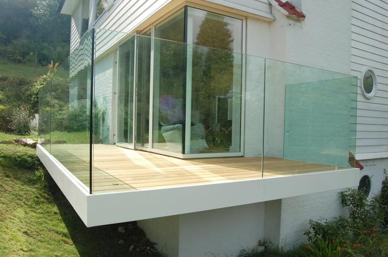Modern house corner with glass sliding doors and a wood deck overlooking a green hillside