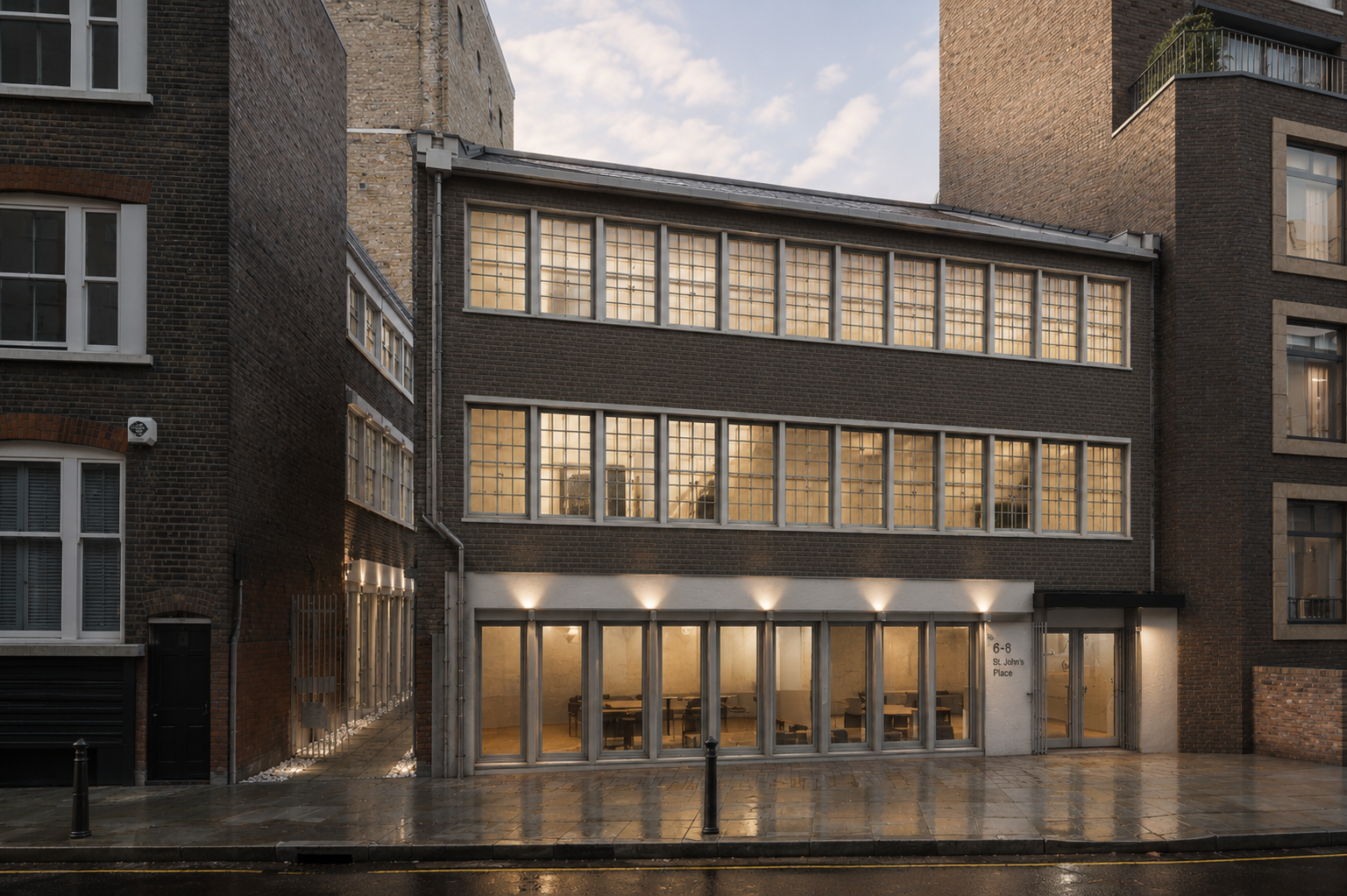 Modern brick building with large windows and lit glass entrance on a wet street at dusk