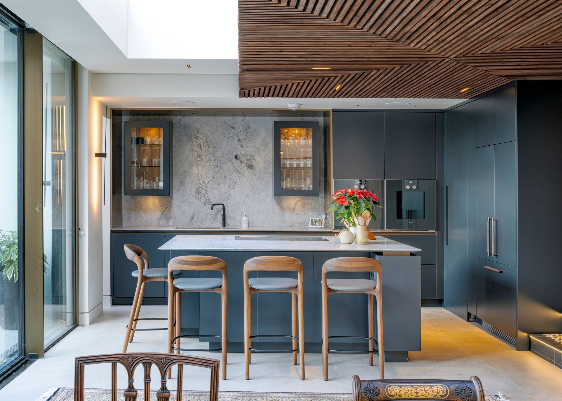 Modern kitchen with dark cabinets, marble island, wooden stools, and a vase of flowers.