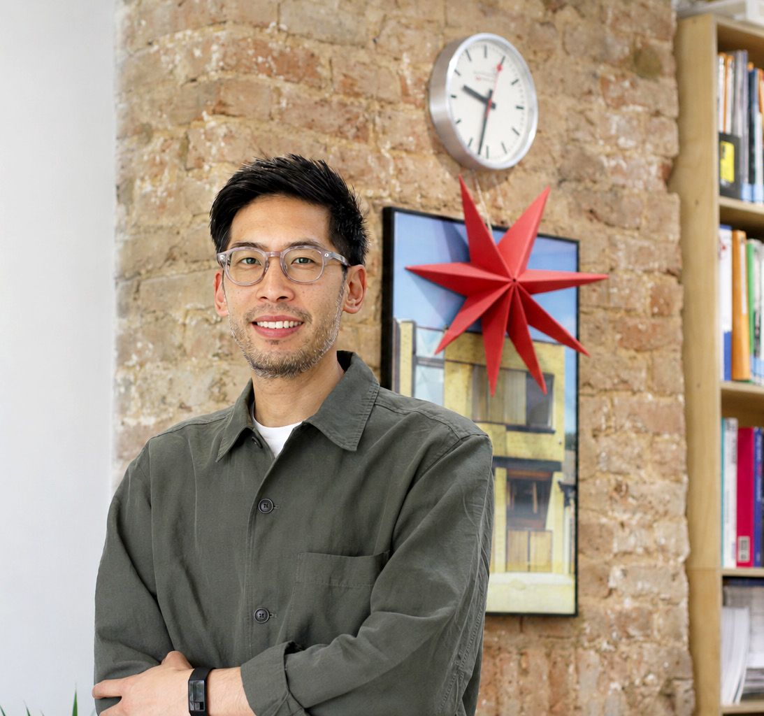 Person standing indoors in front of a brick wall, clock, and red star decoration.