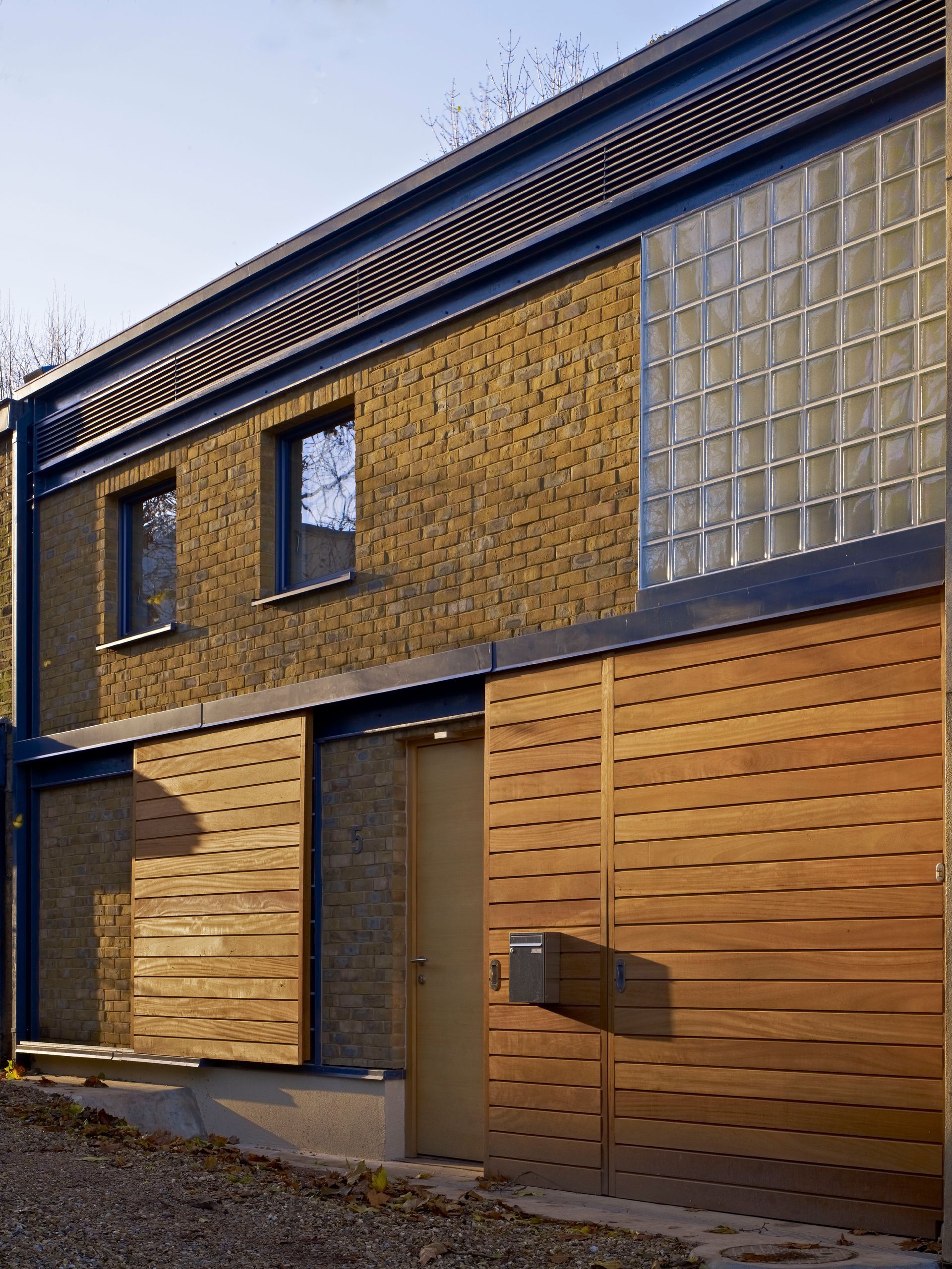Modern two-story brick house with wooden garage doors and a glass-block window wall