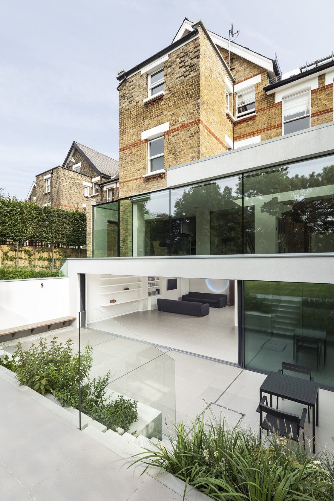 Modern brick house with glass extension, white patio, and small landscaped garden