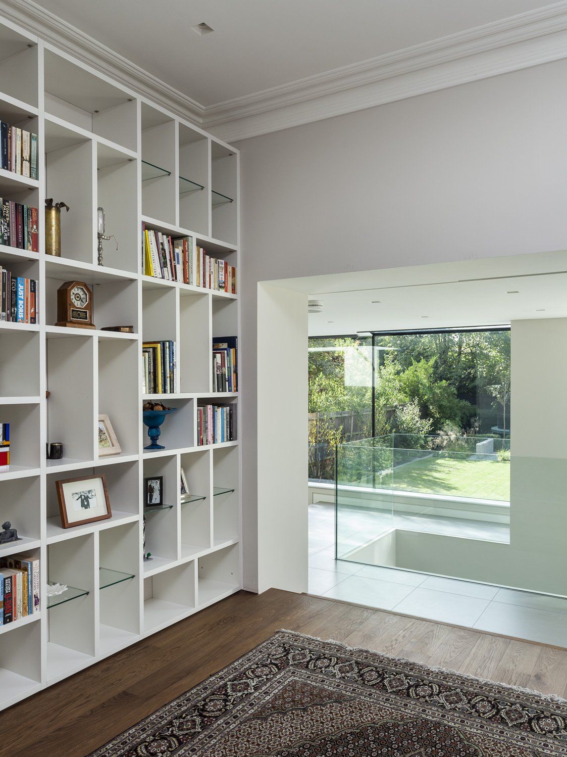 Bright living room with white built-in bookshelves and a glass door opening to a garden and pool.