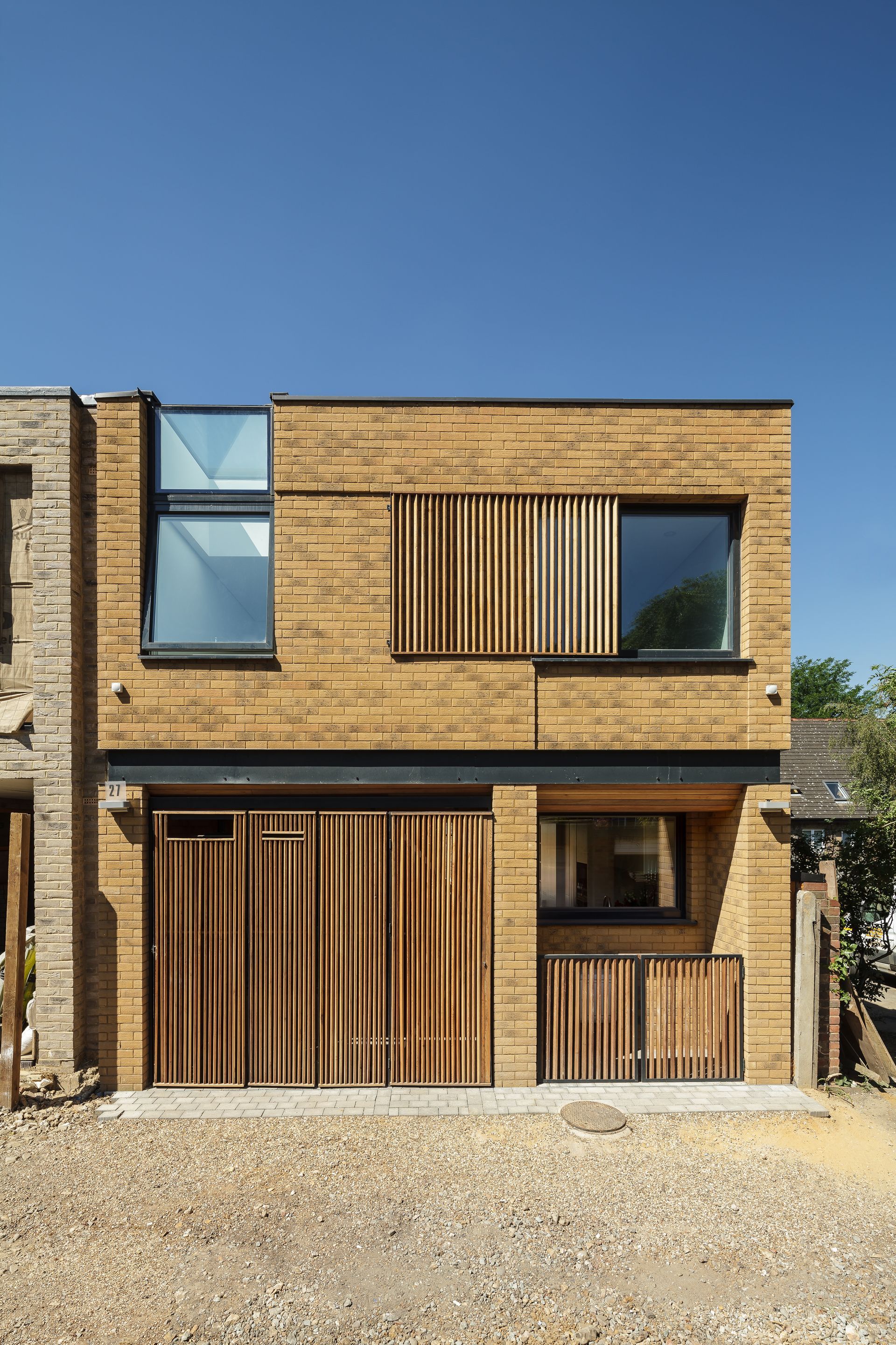 Modern two-story brick house with wood slat shutters and a gravel front yard under a blue sky