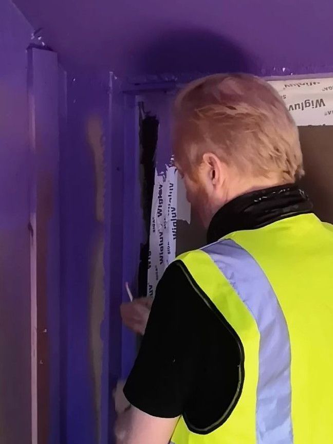 Person in a yellow safety vest inspecting a purple-lit doorway with hanging tape.