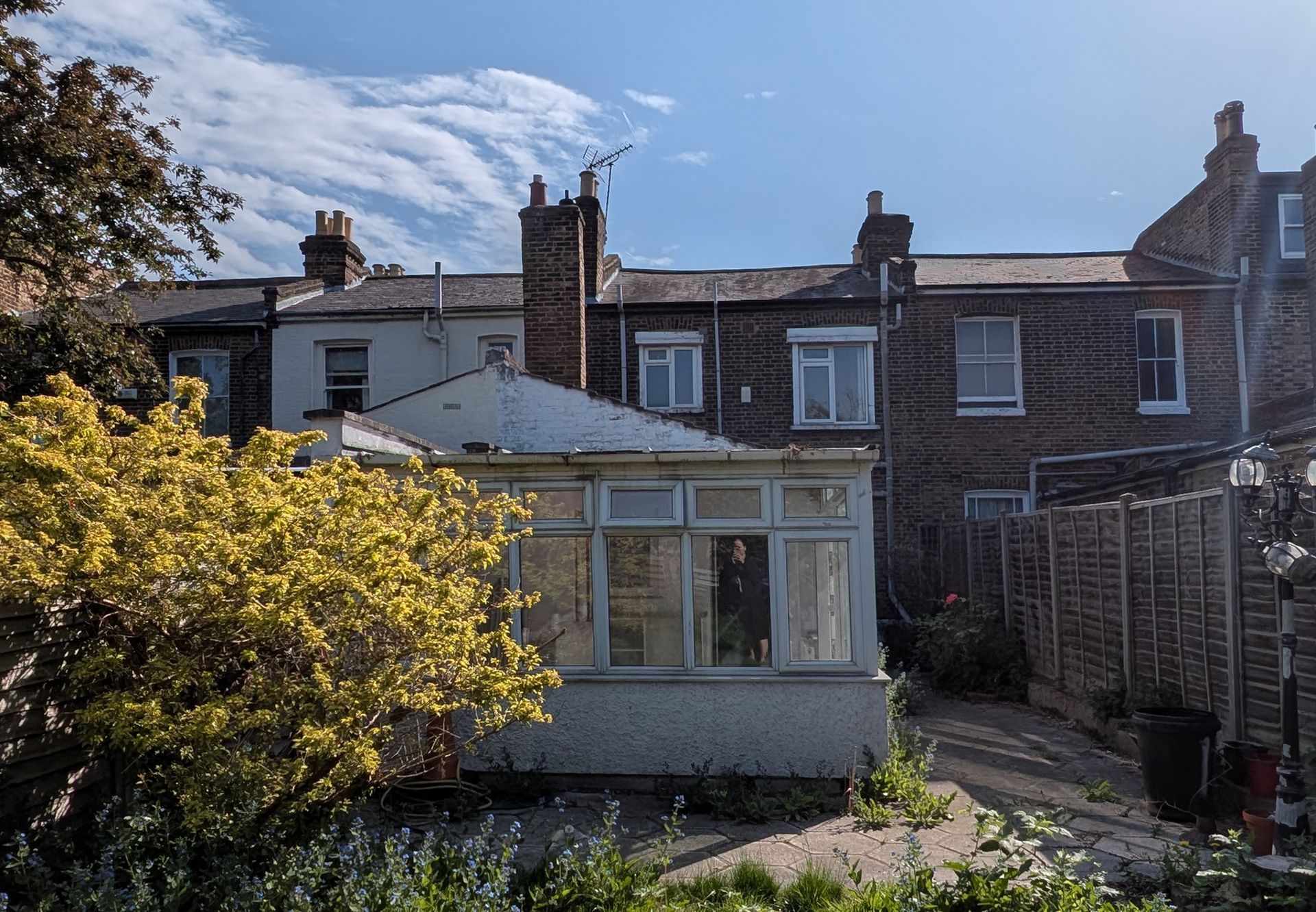 Sunny backyard with a glass sunroom and brick terraced houses behind it