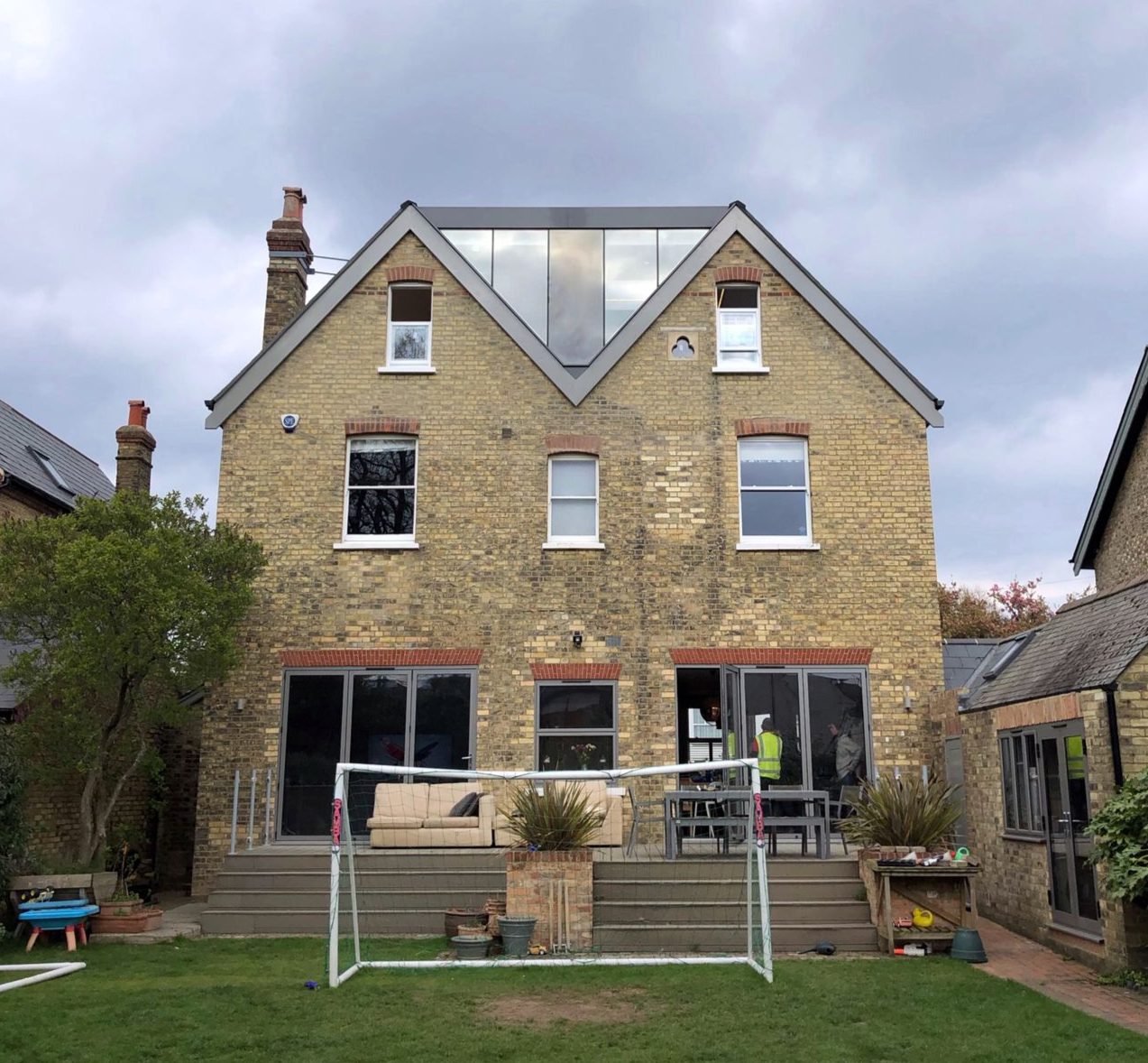 Three-story brick house with dormer windows and a back garden, viewed from the lawn