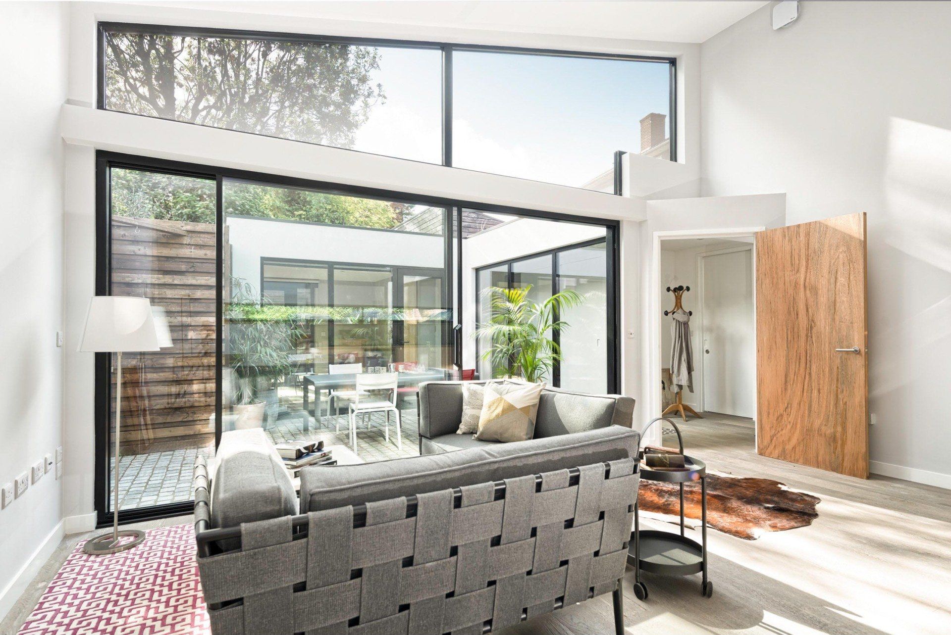 Bright modern living room with gray sofa, large windows, wood accents, and patio doors leading outside