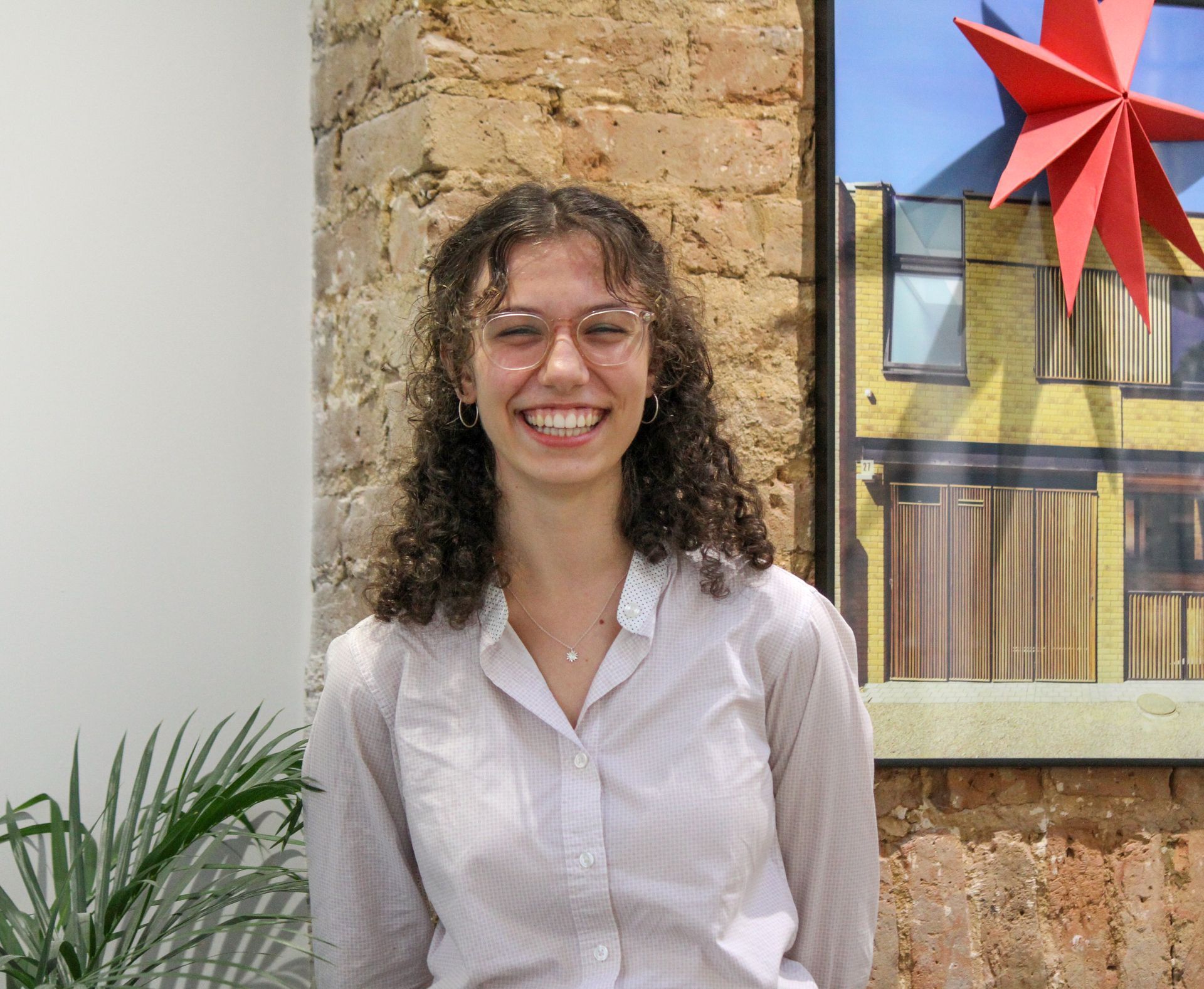 Smiling person with curly hair standing beside a brick wall and red star decoration