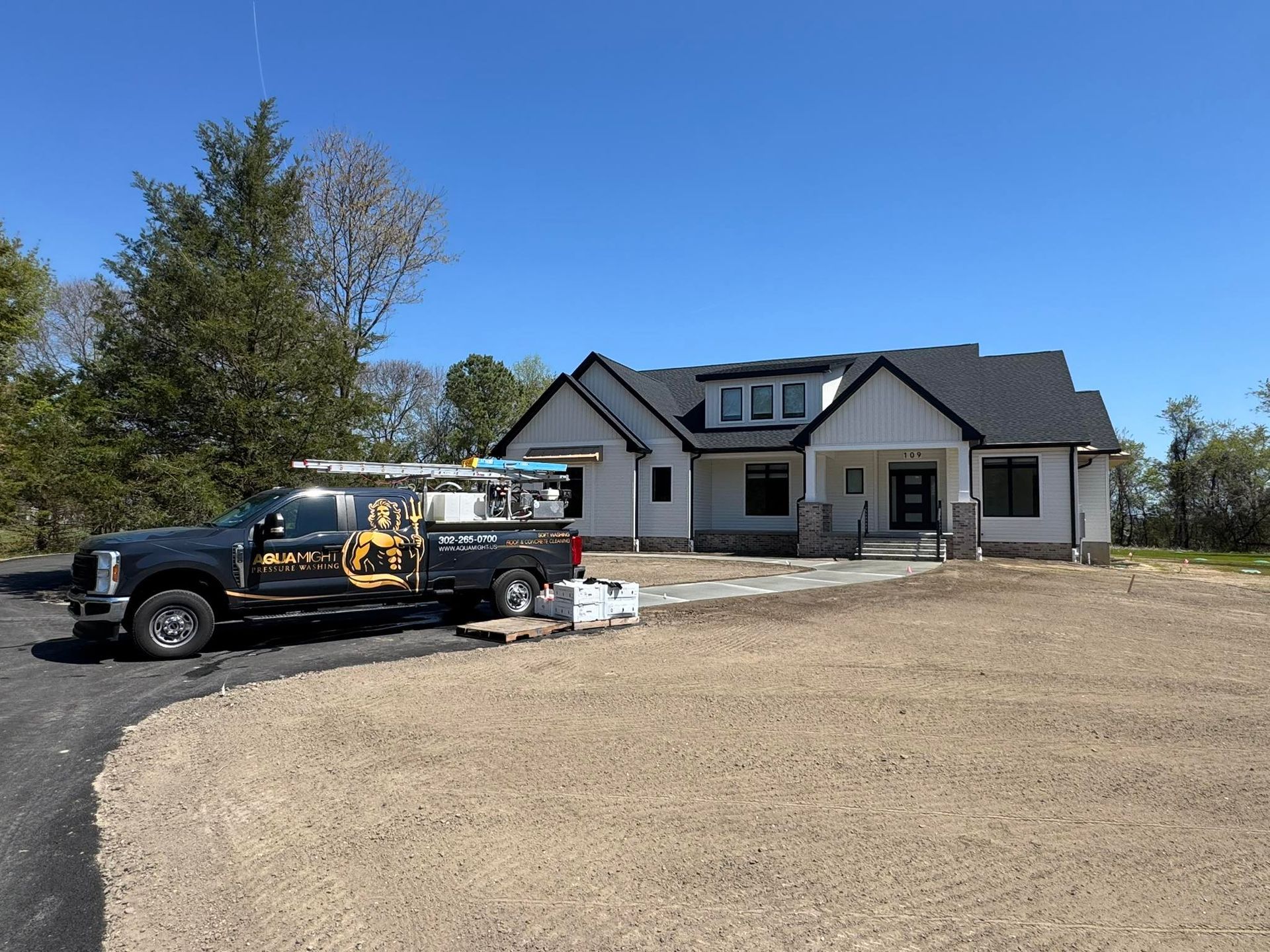 Truck parked in front of a gray house on a dirt lot under a clear blue sky