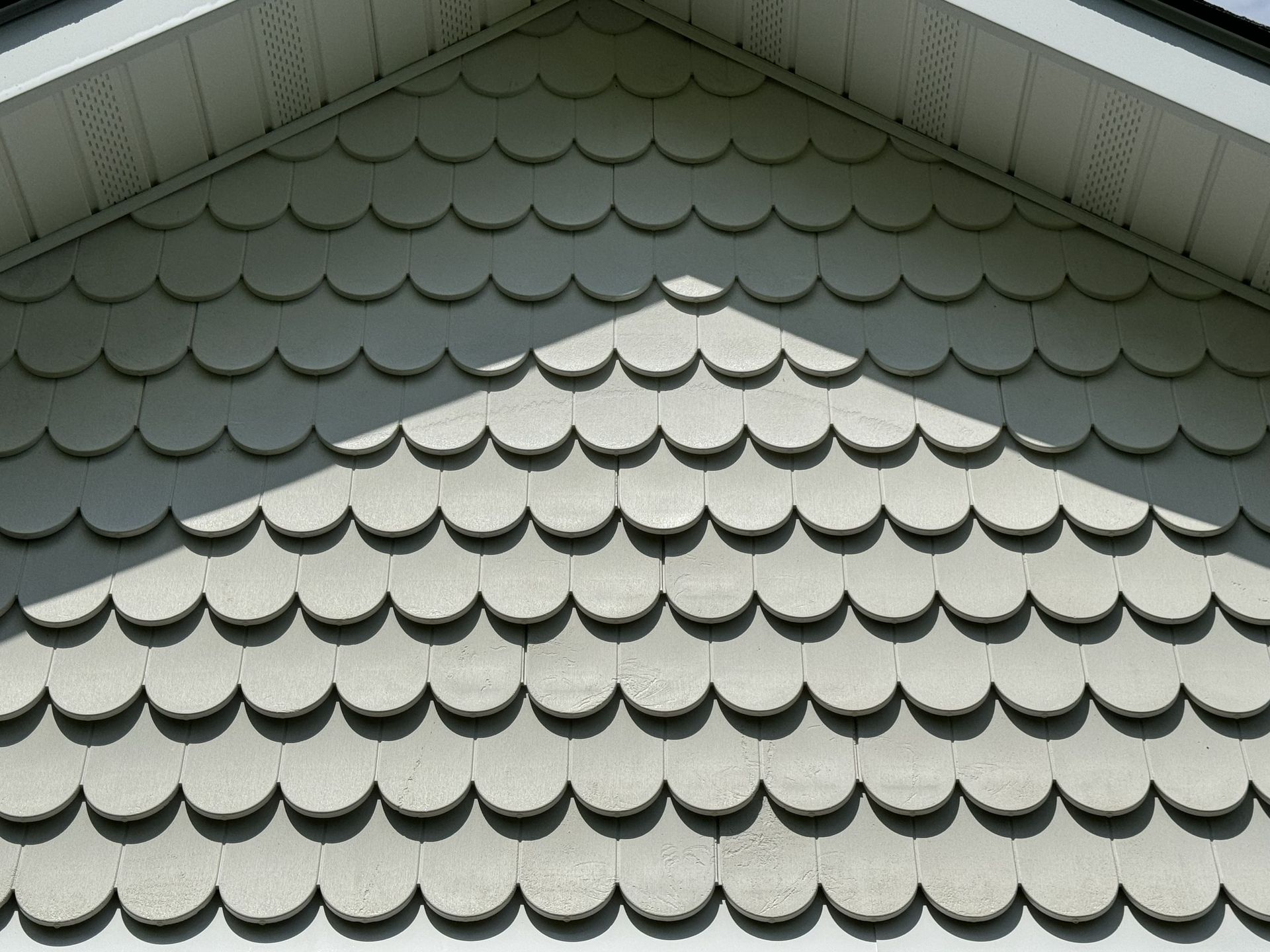 Gray scalloped siding on a triangular gable end of a house, casting shadows.