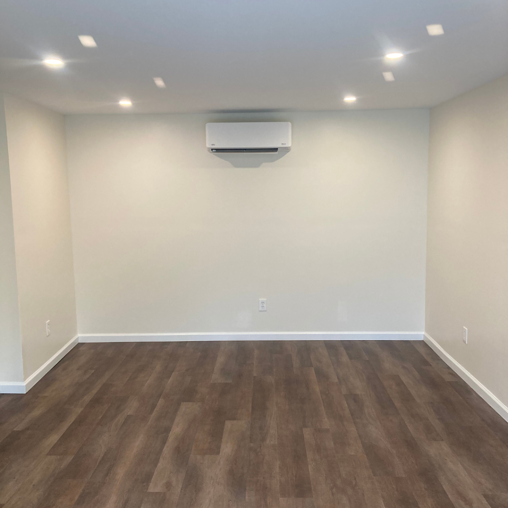 An empty room with hardwood floors and a wall mounted air conditioner.