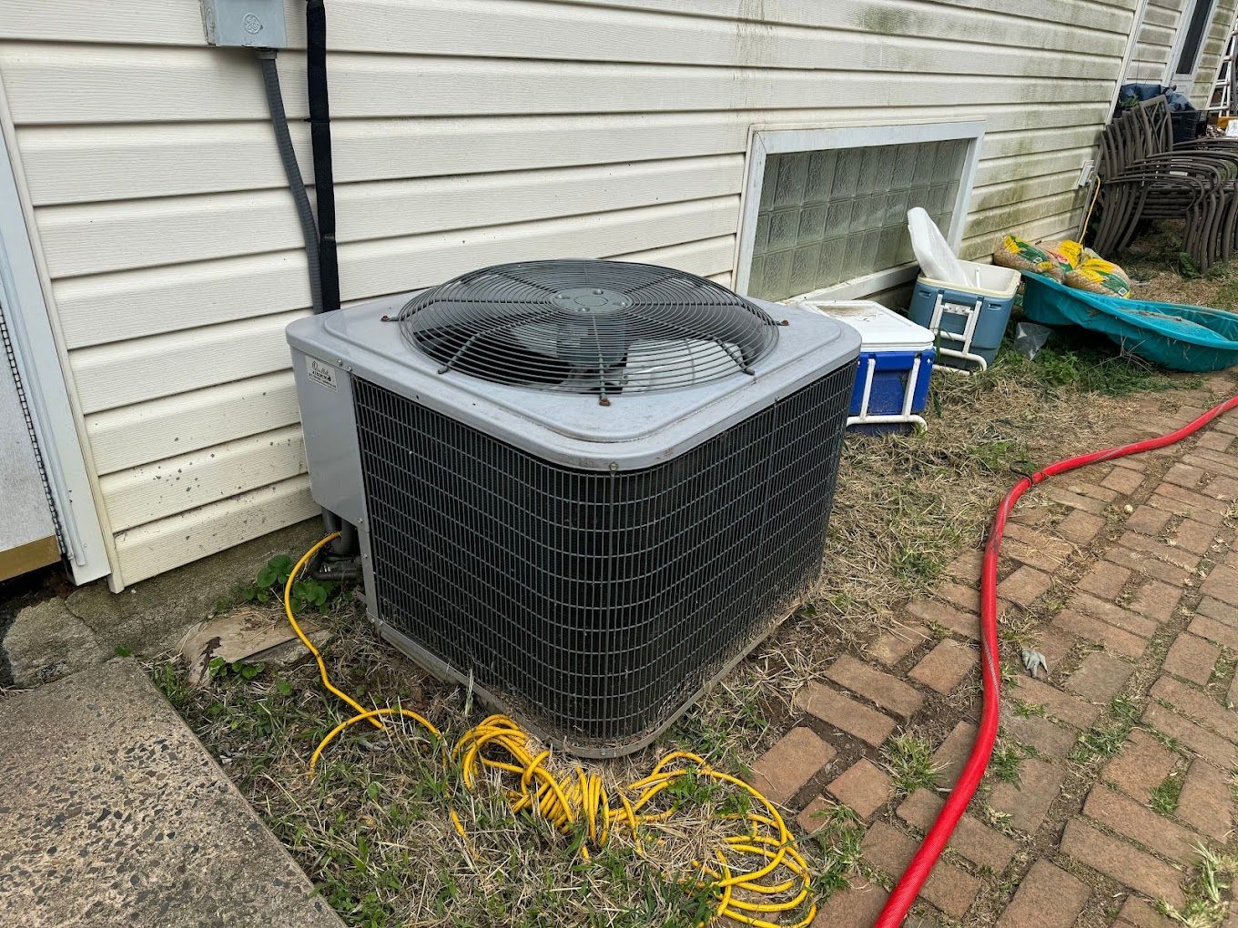 An air conditioner is sitting on the side of a house next to a hose.