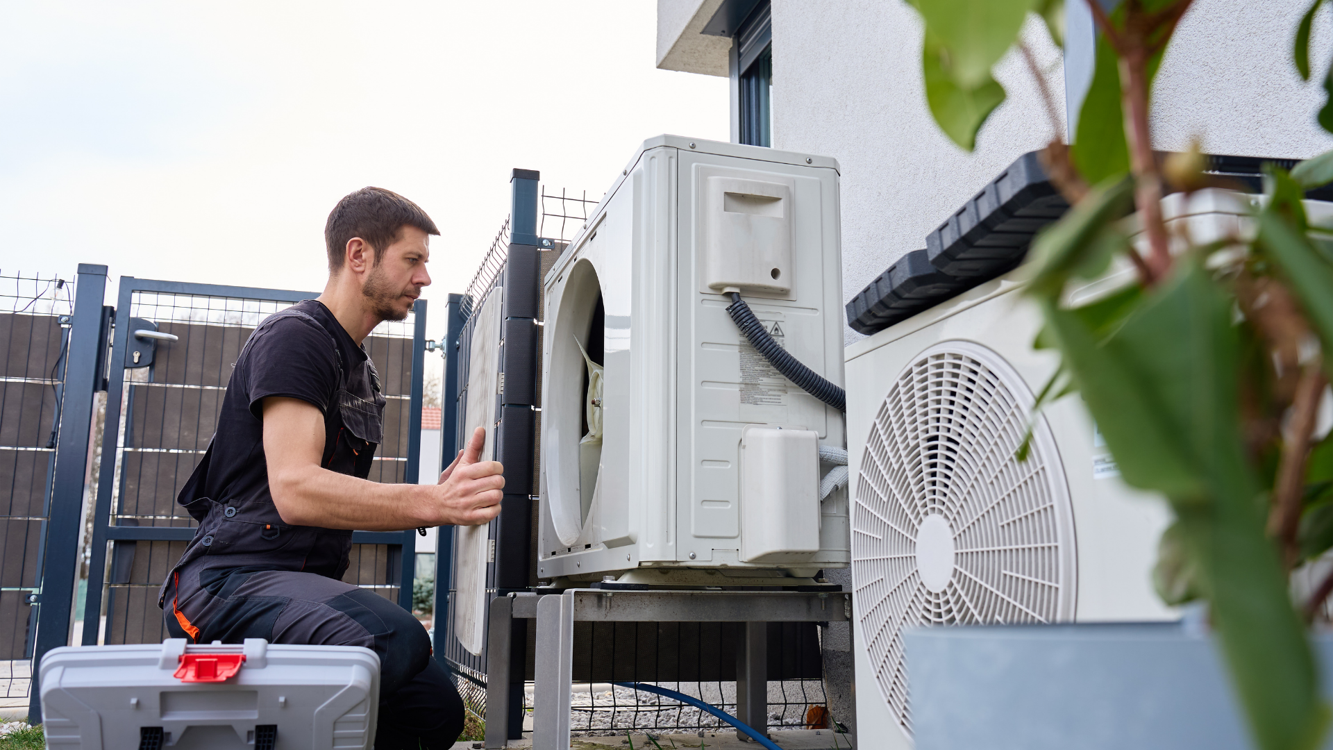 Technician servicing an outdoor air conditioning unit beside a building