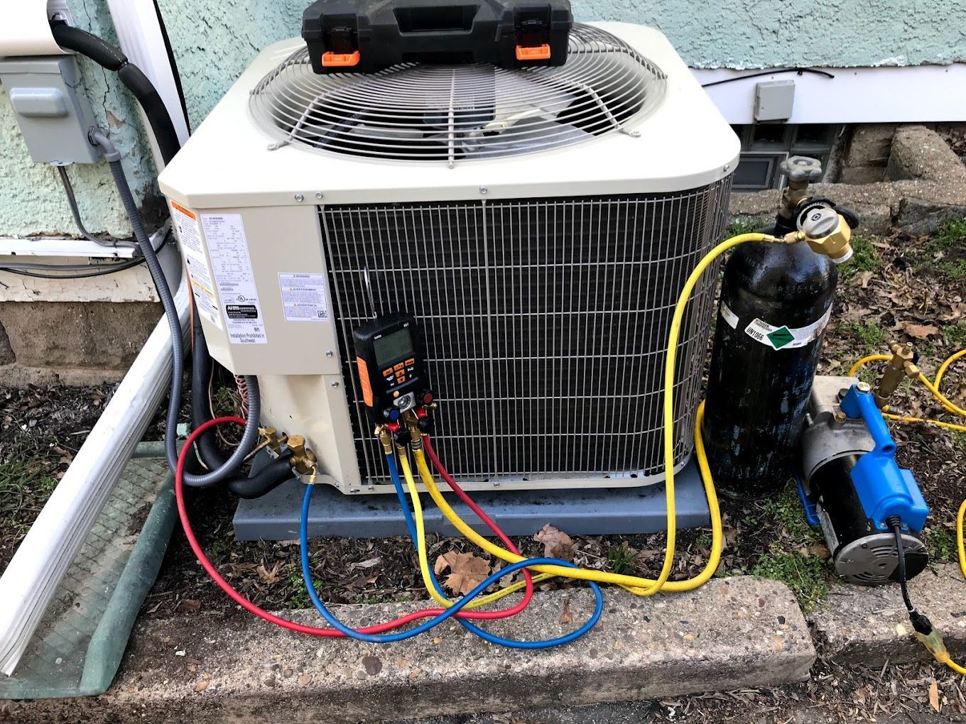 An air conditioner is being serviced outside of a house.