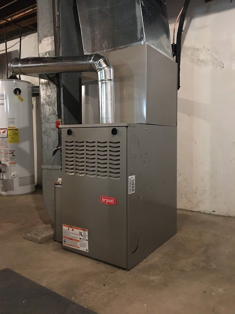 A stainless steel furnace is sitting in a basement next to a water heater.