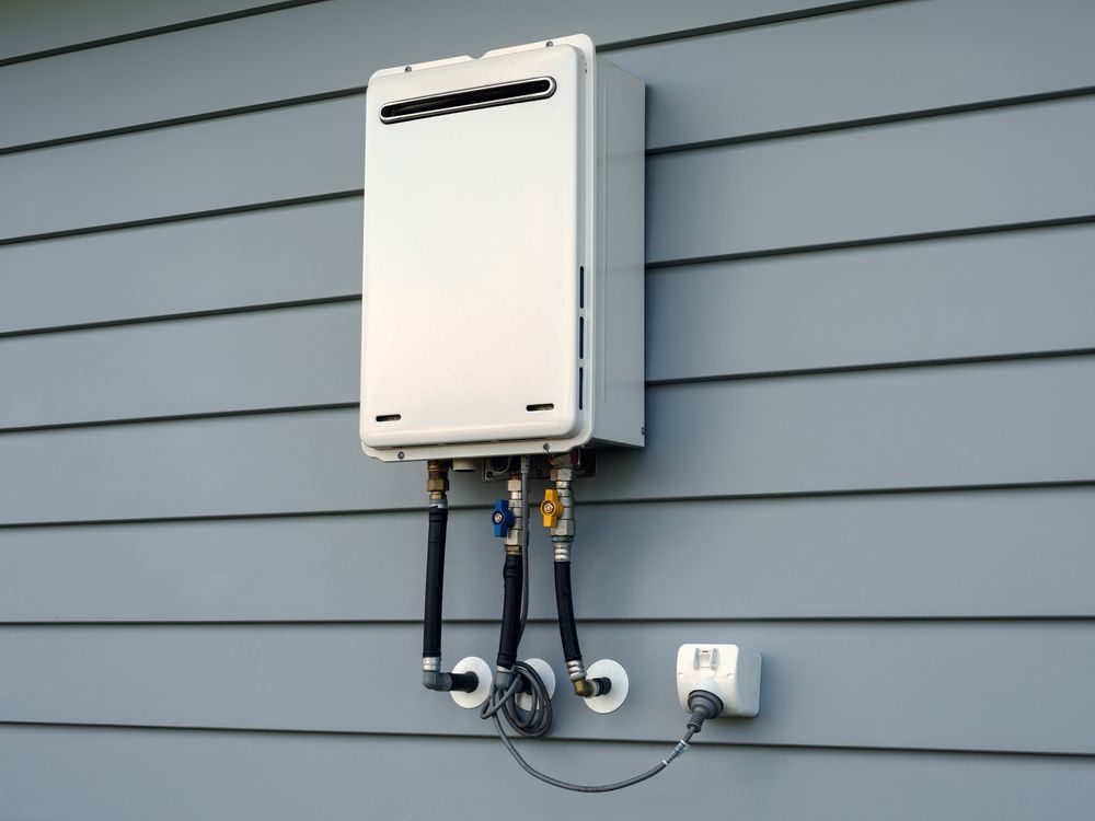 White tankless water heater mounted on gray siding.