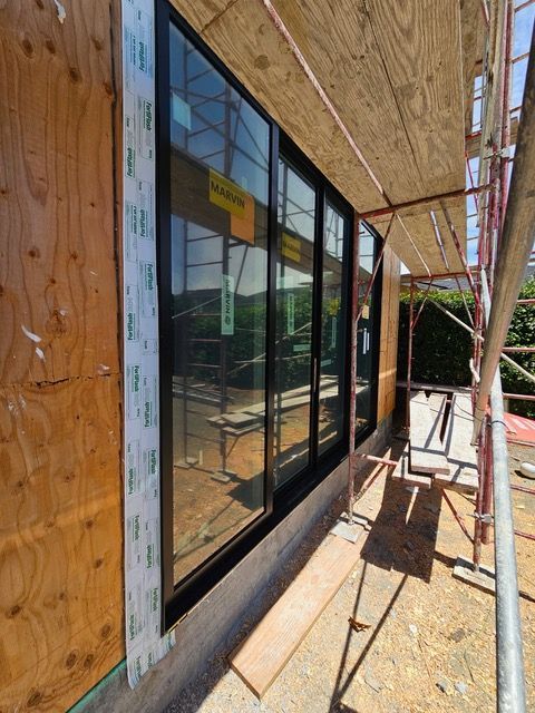 Scaffolding beside a building with black-framed windows and plywood siding in bright sunlight