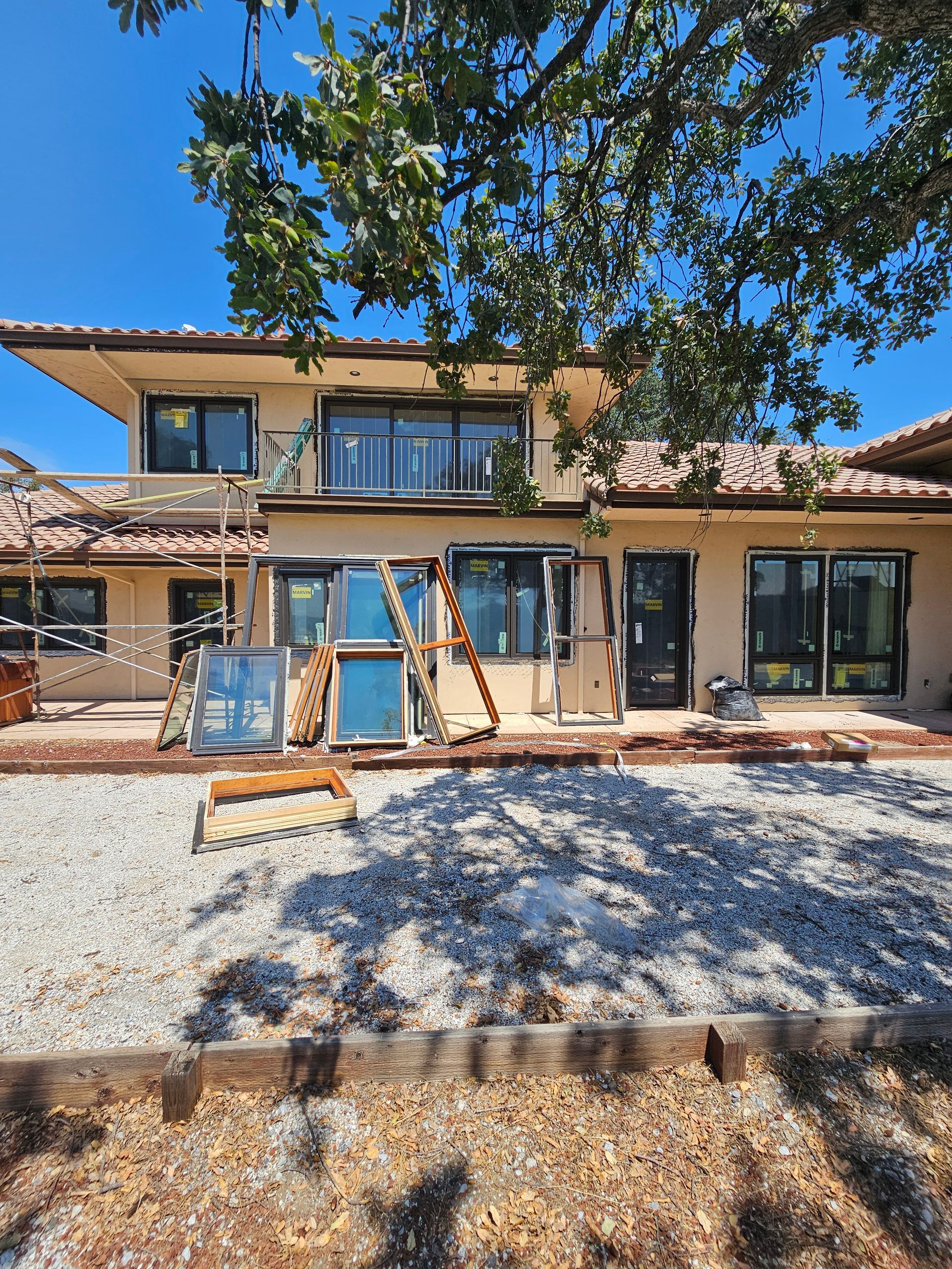 Two-story house exterior with construction materials and gravel yard under a clear blue sky